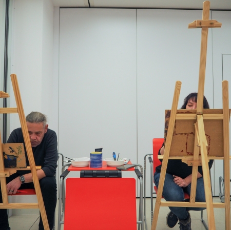 Dwie osoby widziane zza sztalug i malujące.