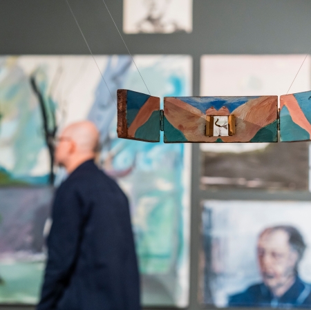 mężczyzna idący w przestrzeni wystawy. W tle szereg, różnorodnych, powieszonych obrazów.