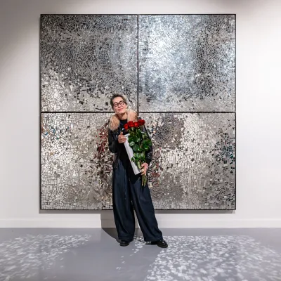 A person with flowers standing in front of a work containing mirror fragments