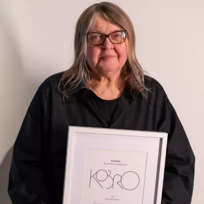 A person with glasses holding a diploma framed in a white frame